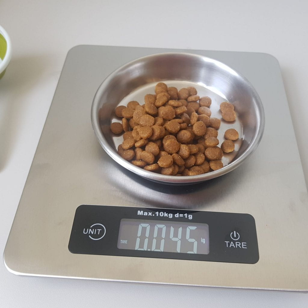A tin bowl of kibble on a gram scale. 