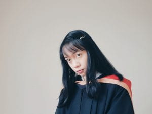 A photo of Tesa in her convocation gown. The gown is black. The convocation hood is red with a gold stripe on the inner edge. 